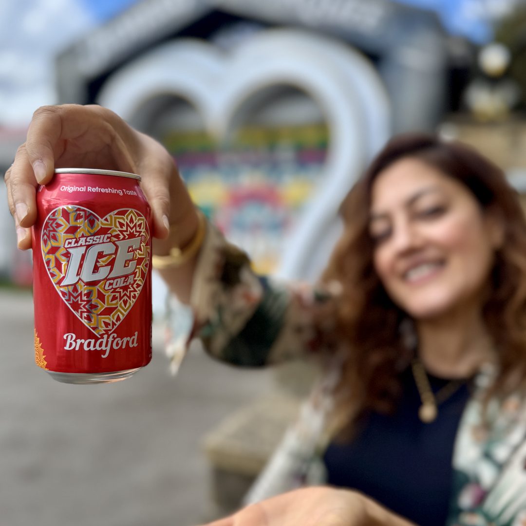A customer holding up a branded Bradford drink can in front of a city landmark.