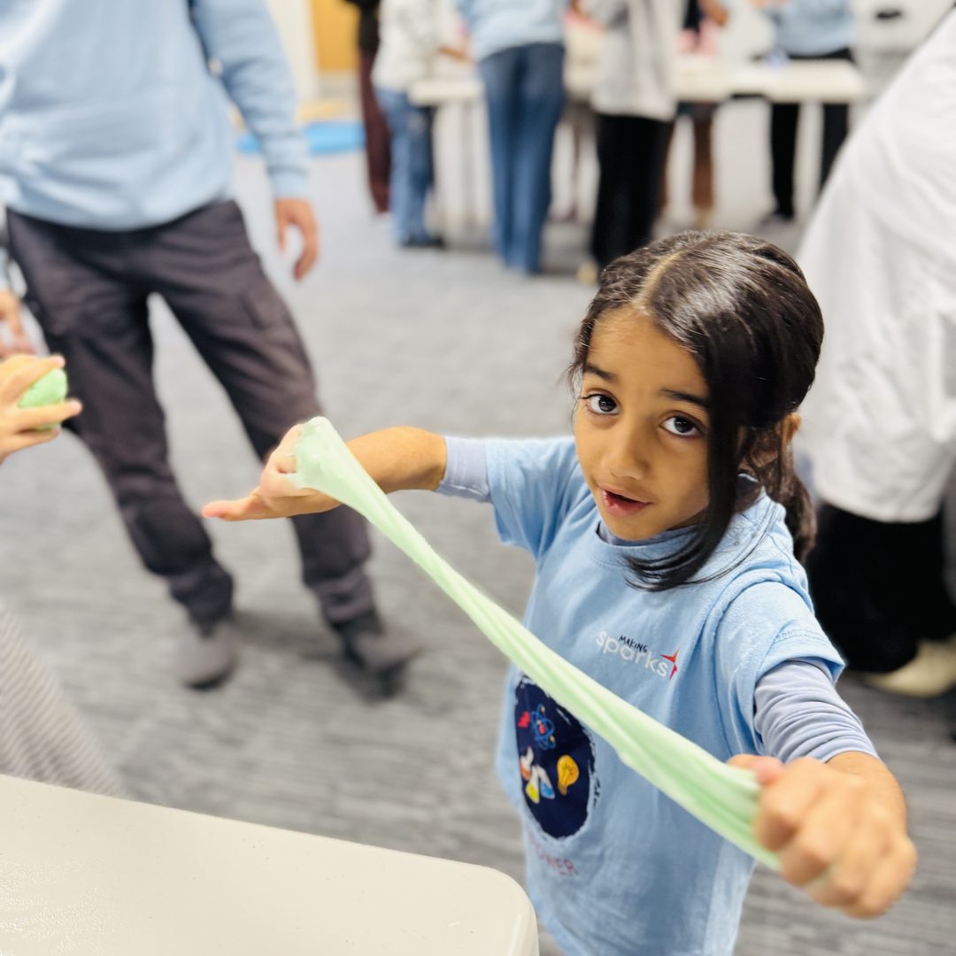 A child stretching slime between both hands at a Making Sparks hands-on science session.